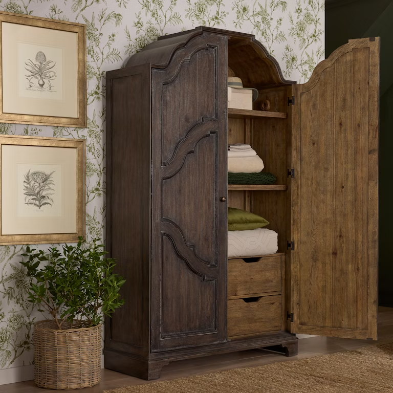 The Revival Row 2-Door Armoire, featuring a dark Chimney Smoke finish, offers four drawers and adjustable shelving behind two doors. Crafted from hickory veneers, this traditional-style armoire blends English and French design elements with modern functionality, making it a versatile storage solution for any space.