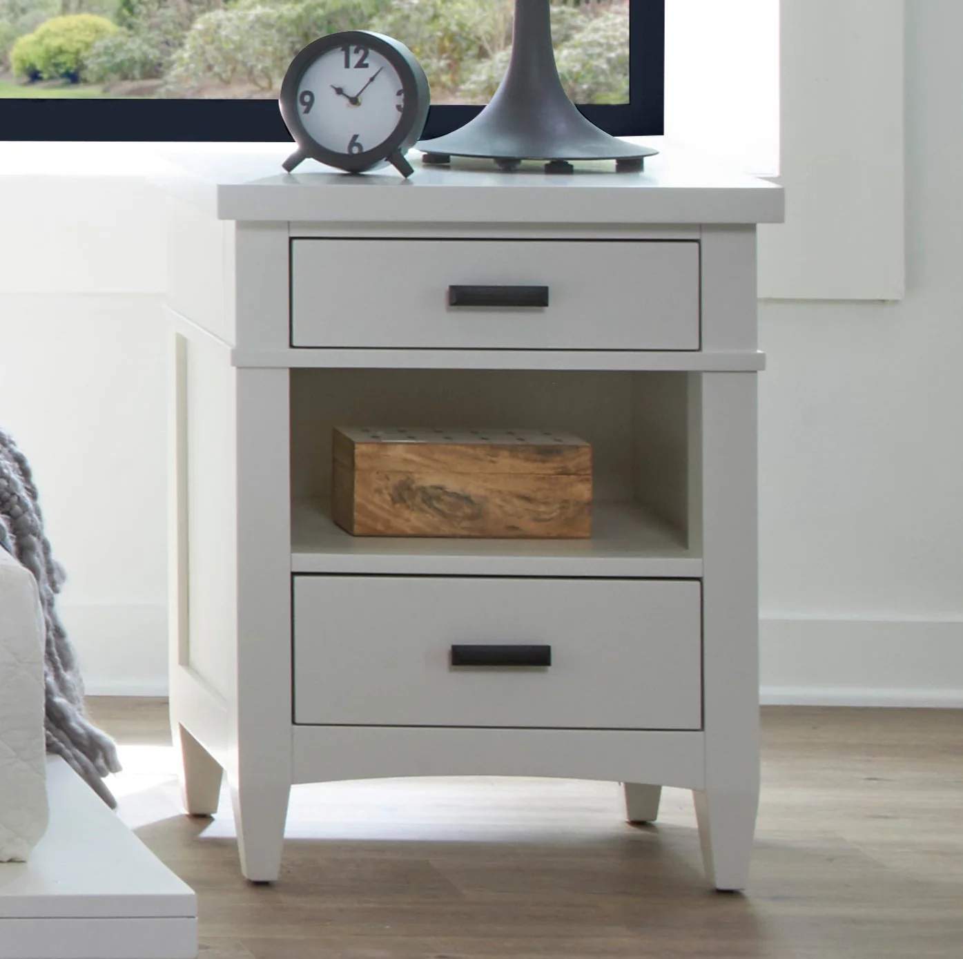 The Americana Modern 2-Drawer Nightstand offers timeless style with a fresh Cotton finish and Burnished Bronze hardware. Crafted from poplar solids and birch veneers, it features two drawers and an open shelf for storage. With tapered legs and smooth drawer glides, this durable piece is perfect for smaller spaces.