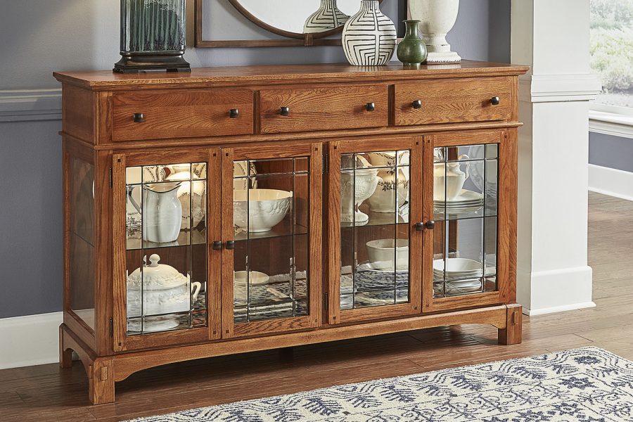 A-America buffet crafted from solid oak with a light brown medium wood tone finish, antique bronze hardware, and distressed details. Dimensions: 66W x 19D x 41H, providing a durable and stylish storage solution for dining spaces.