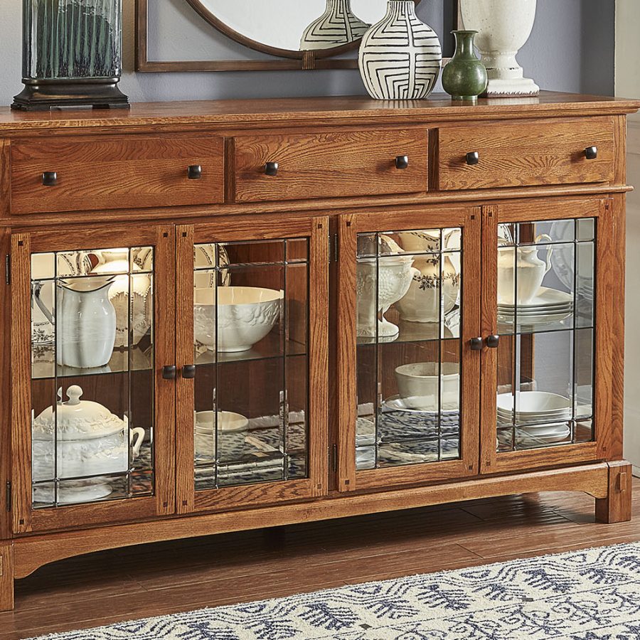 A-America buffet crafted from solid oak with a light brown medium wood tone finish, antique bronze hardware, and distressed details. Dimensions: 66W x 19D x 41H, providing a durable and stylish storage solution for dining spaces.